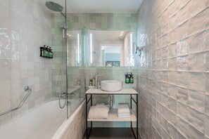 A modern bathroom with a bathtub, a glass-enclosed shower, a white sink, and a mirror. - voco Paris Montparnasse by IHG (Paris)