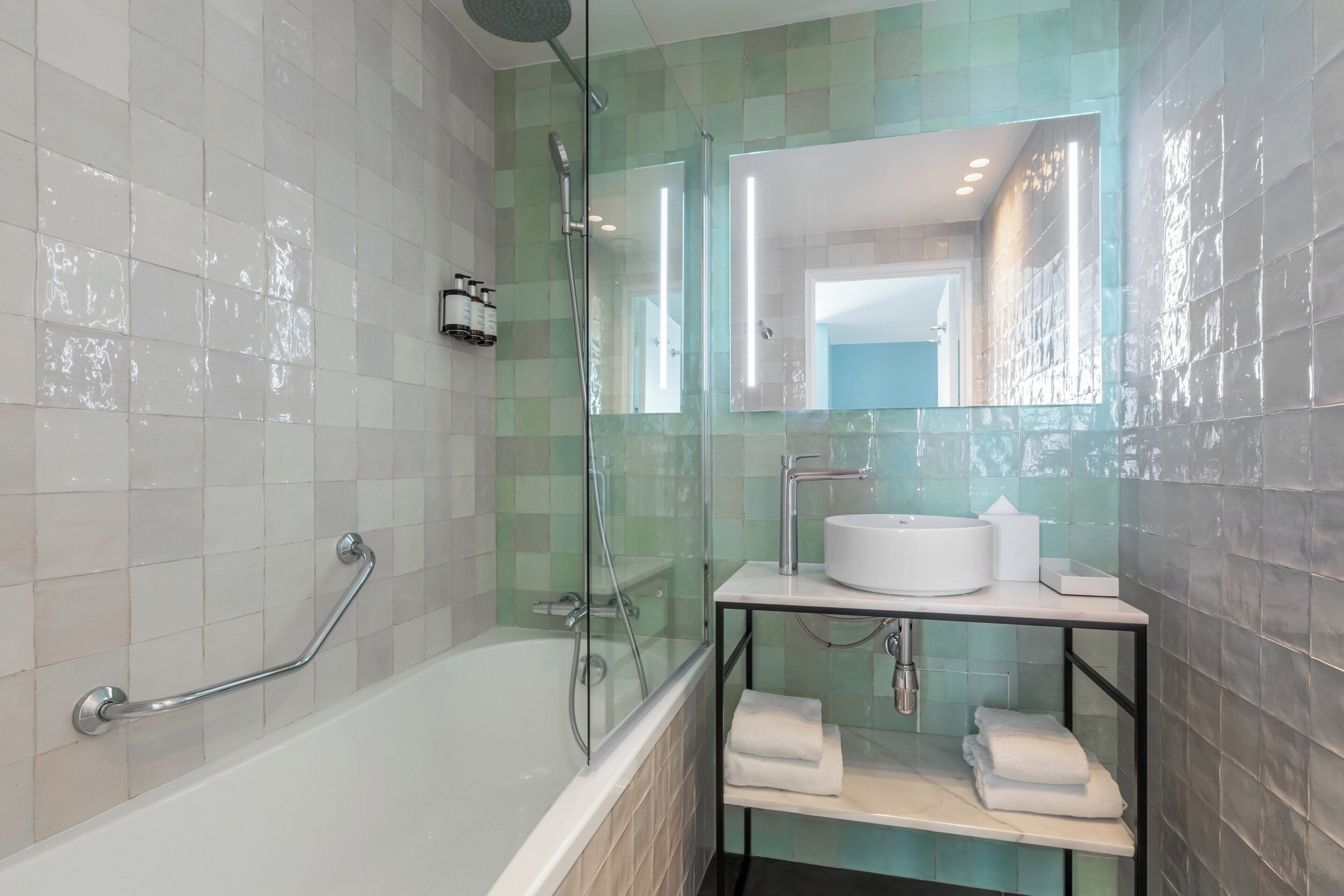 Un baño moderno con bañera, cabina de ducha con mampara de vidrio y tocador con lavamanos y toallero.