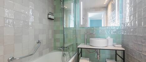 Un baño moderno con bañera, cabina de ducha con mampara de vidrio y tocador con lavamanos y toallero.