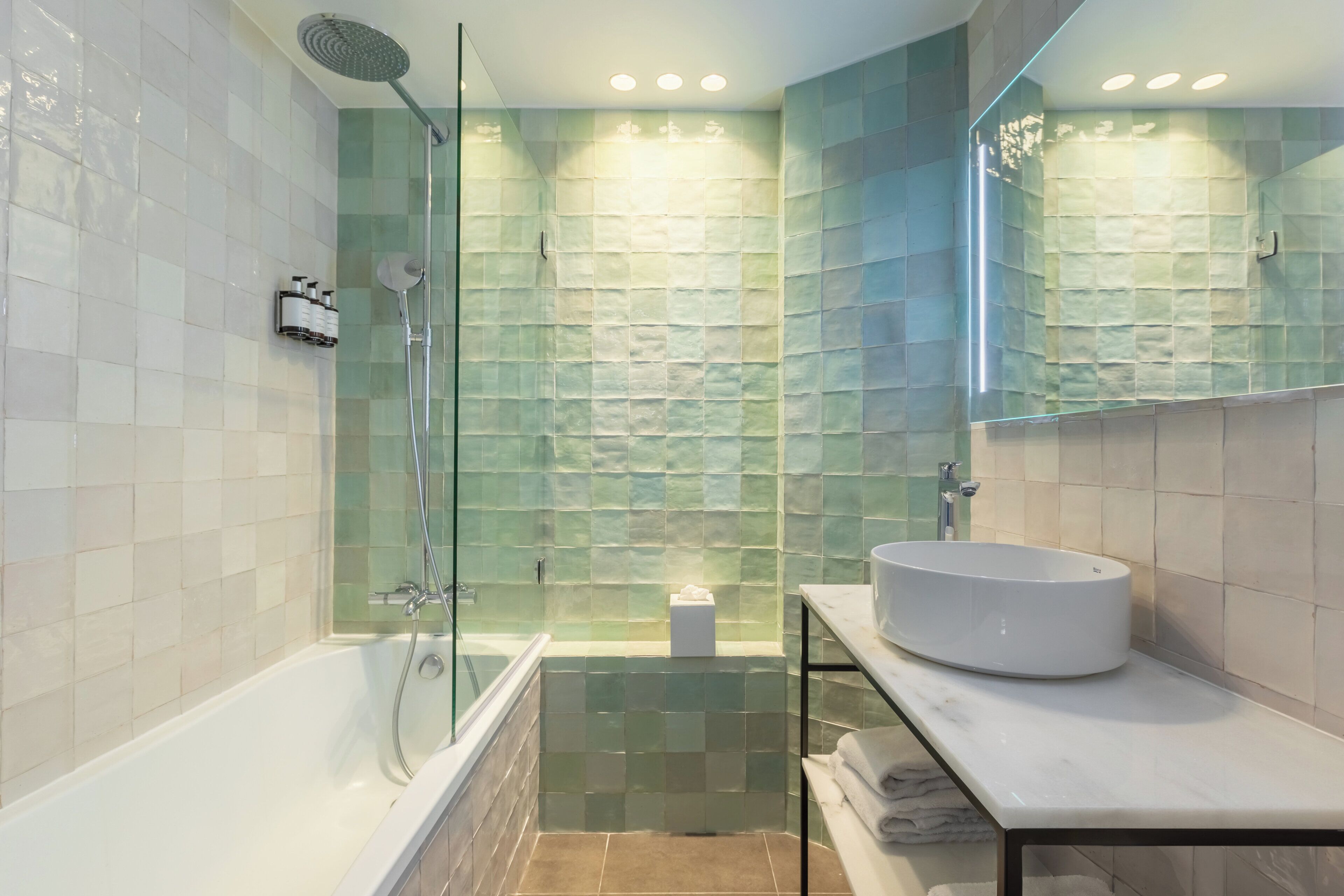 A modern bathroom with a glass-enclosed shower, a white bathtub, and a marble countertop with a sink.