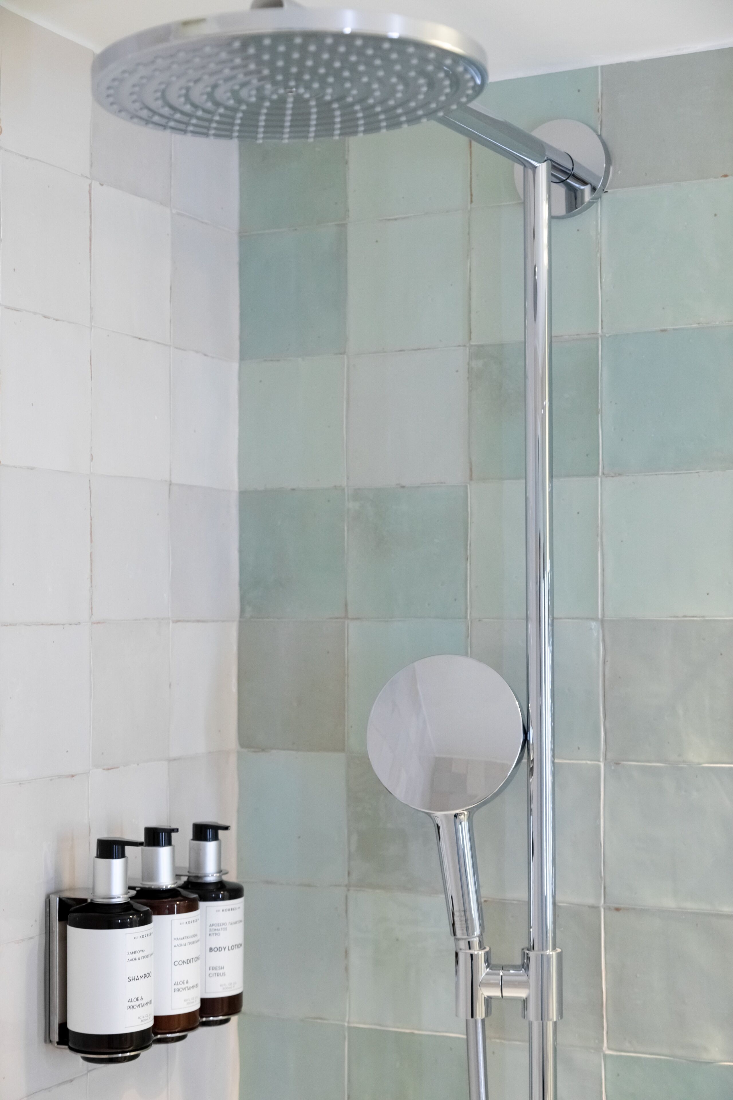 Een douche met een handspiegel en een fles shampoo, conditioner en bodylotion aan de muur.