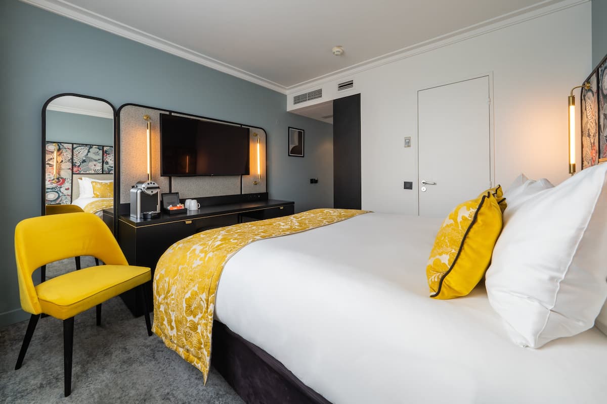 A hotel room with a bed, a desk, a chair, a television, and a door.