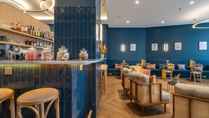 Un'area bar con sgabelli, un bancone pieno di bottiglie e una zona salotto con divani e poltrone.