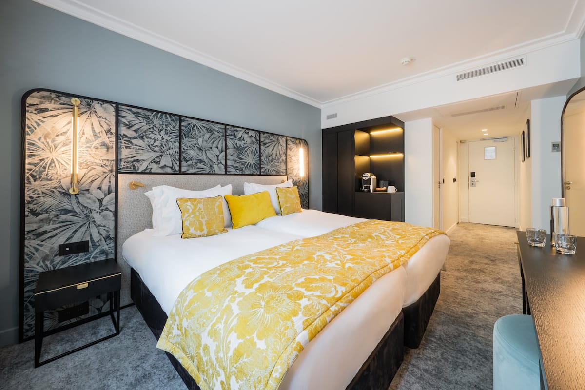 A modern hotel room with a large bed, a bedside table, a nightstand, and a built-in shelf with toiletries.