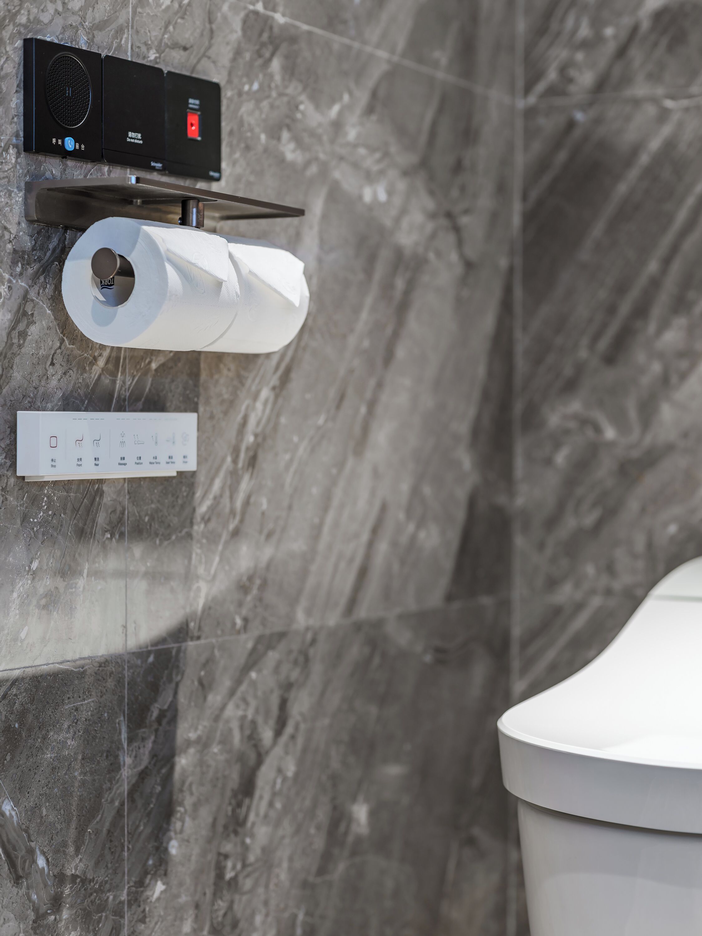 A toilet paper holder with a roll, a flush button, and a control panel with a red indicator light.