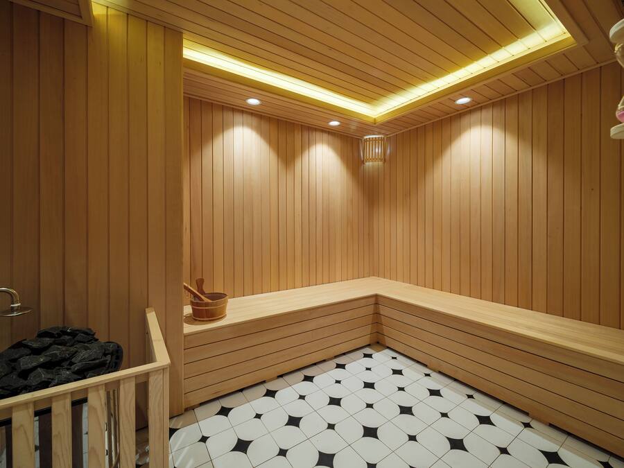 A sauna room with wooden walls and benches, a tiled floor, and a wooden bucket.