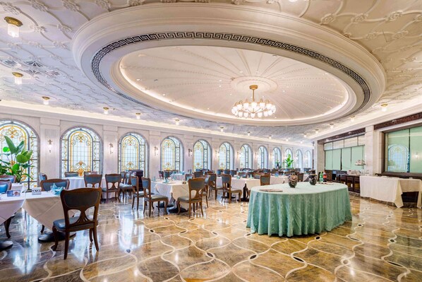 A spacious banquet hall with ornate ceiling, large windows, and a central chandelier.
