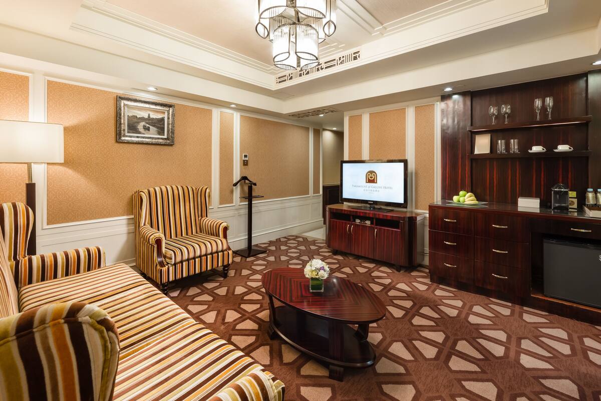 A hotel room with striped sofas, a coffee table, a TV, a minibar, and a patterned carpet.