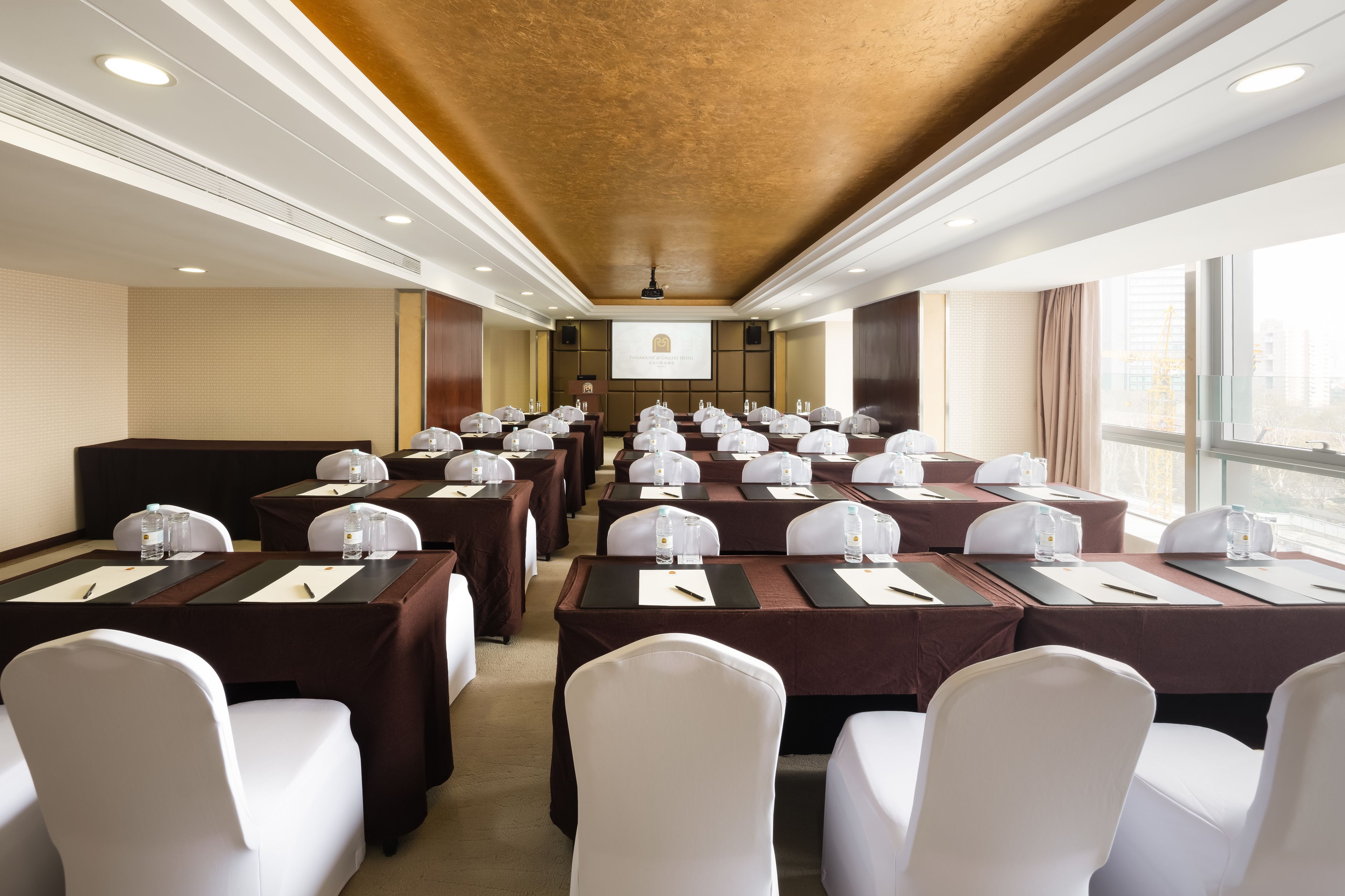 A conference room with multiple tables, white chairs, and a projector screen at the front.