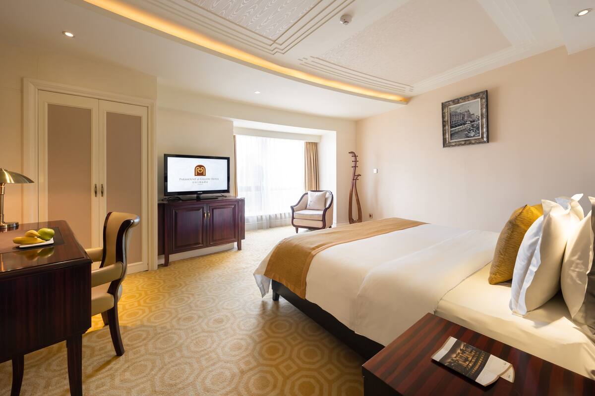 A hotel room with a bed, a desk with a lamp, a television, and a chair.