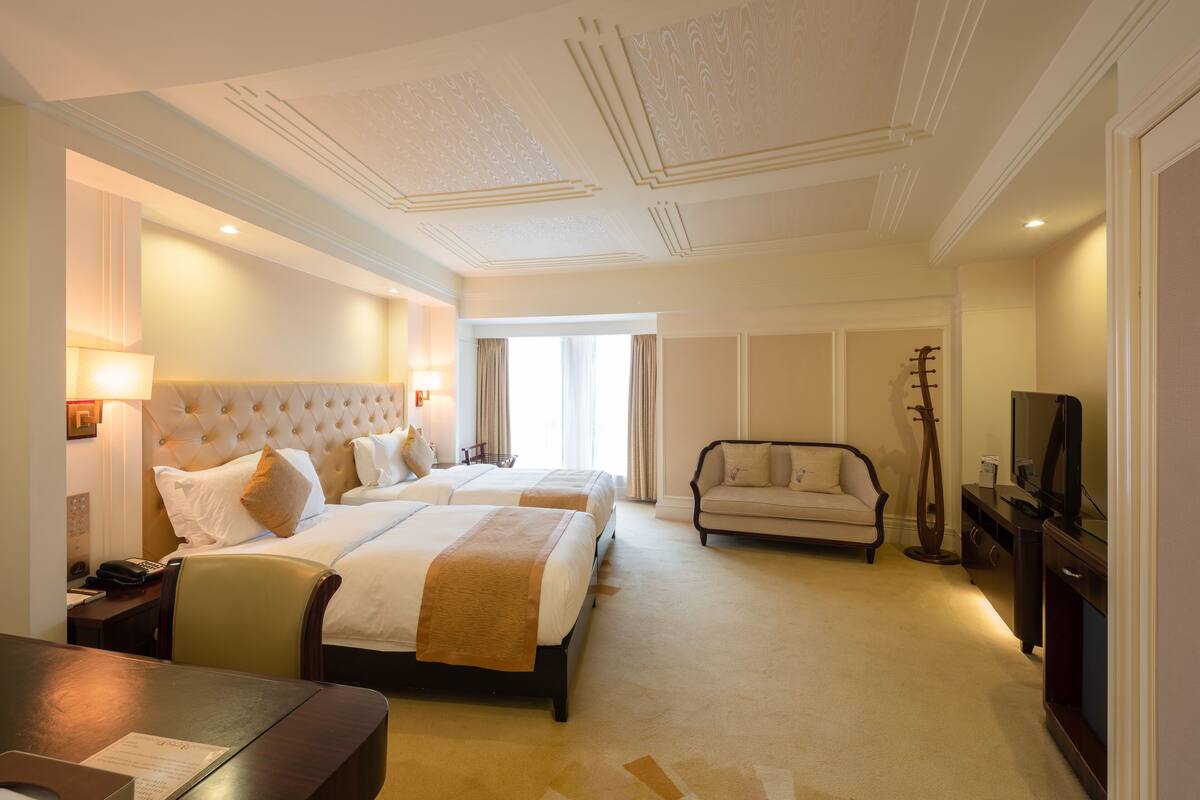A hotel room with two beds, a sofa, a television, and a desk.