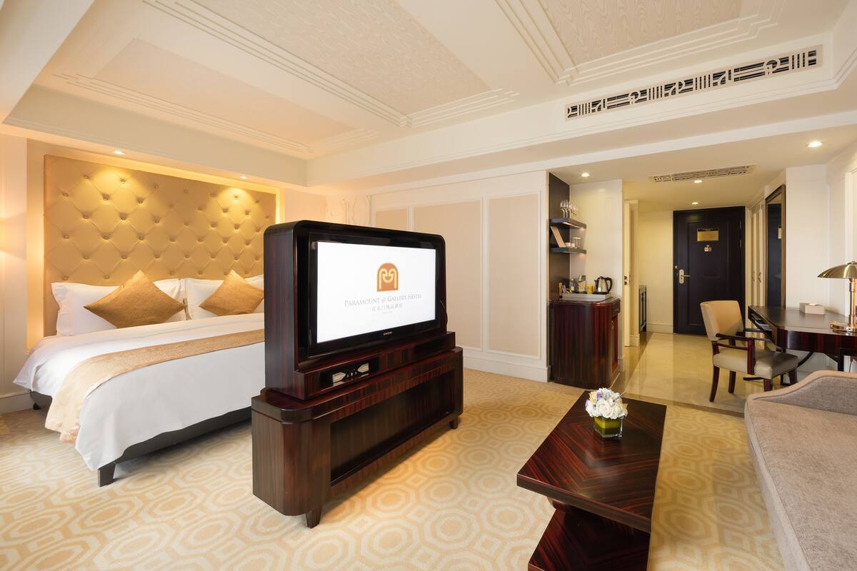 A hotel room with a large bed, a television, a wooden coffee table, and a desk with a chair.
