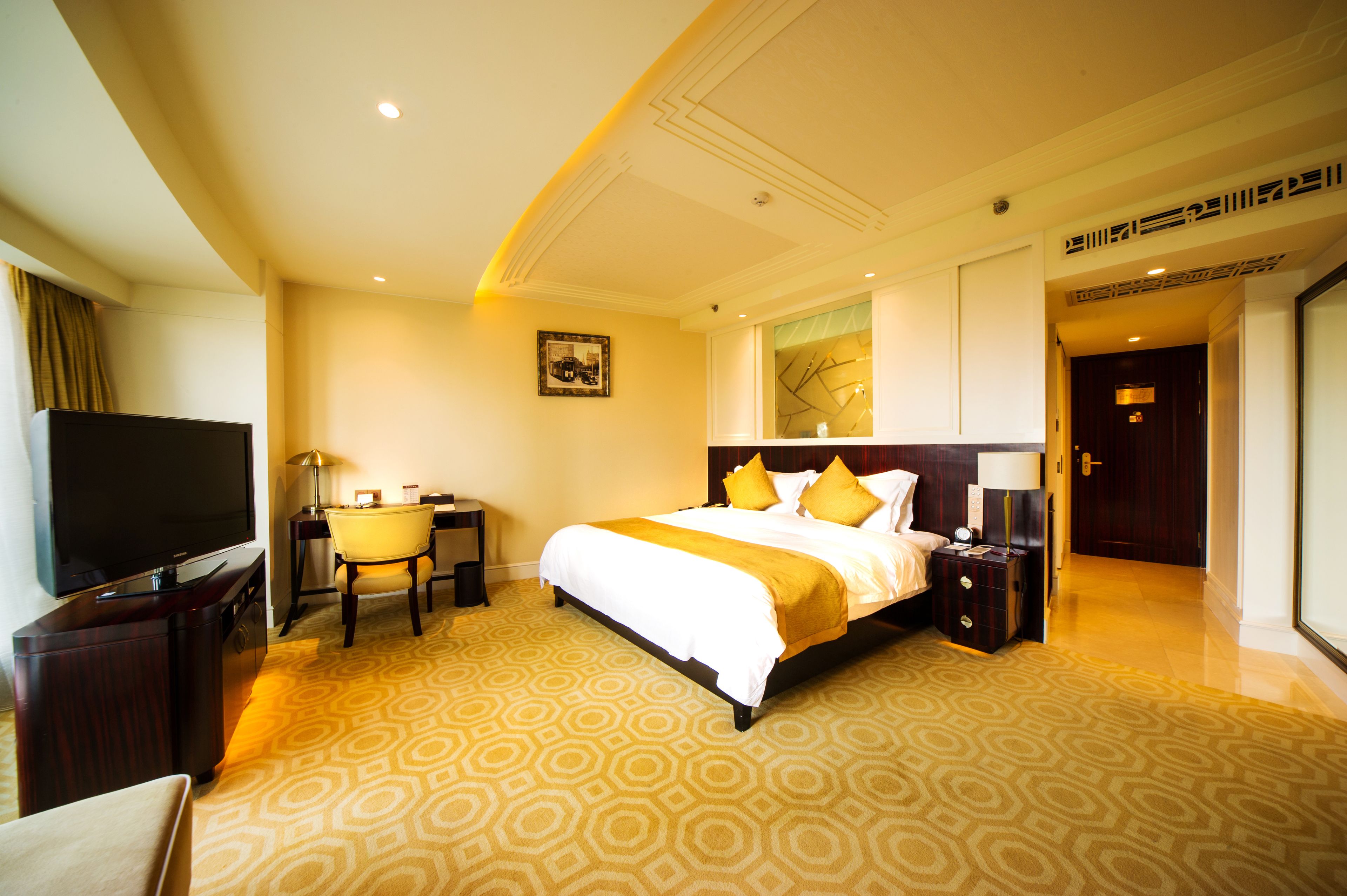 A hotel room with a large bed, a desk, a television, and a view of the outside.
