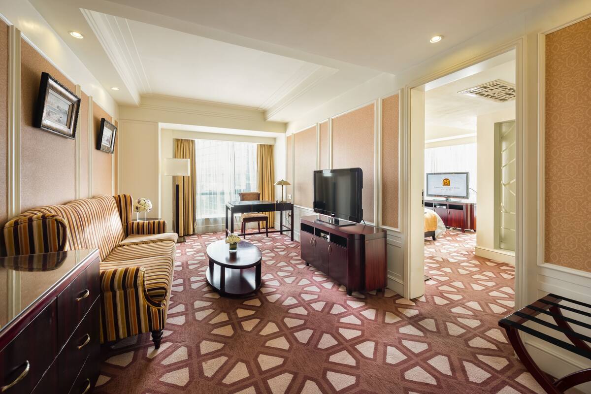 A hotel room with a sofa, TV, and a patterned carpet.