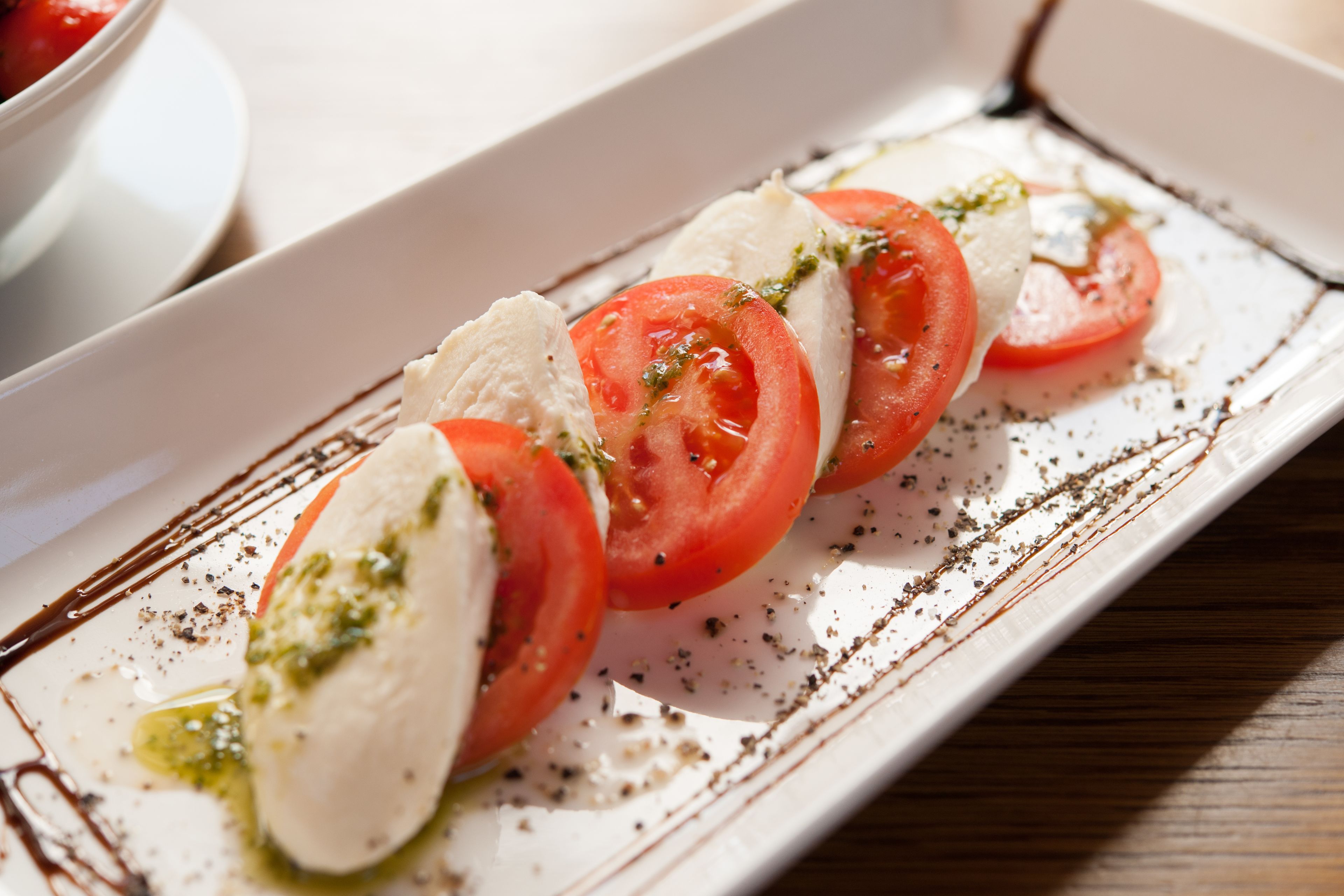 A white rectangular plate with mozzarella and tomato slices, garnished with herbs and olive oil.
