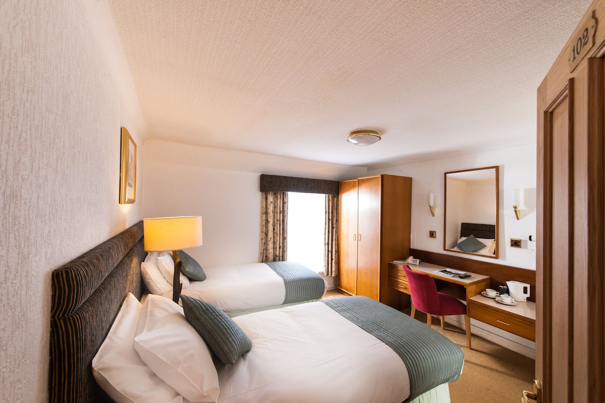 A hotel room with two beds, a desk, a chair, a wardrobe, and a mirror.