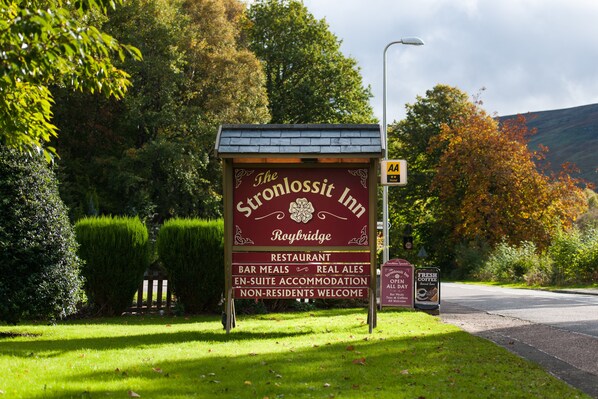 A sign for The Sconnositt Inn in Roybridge, advertising a restaurant, bar meals, real ales, en-suite accommodation, and welcoming non-residents.