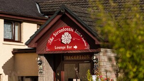 L’auberge Stronlossit, reconnaissable à son panneau « Bar-salon », à la porte de la réception et à son mur de pierre orné de plantes.