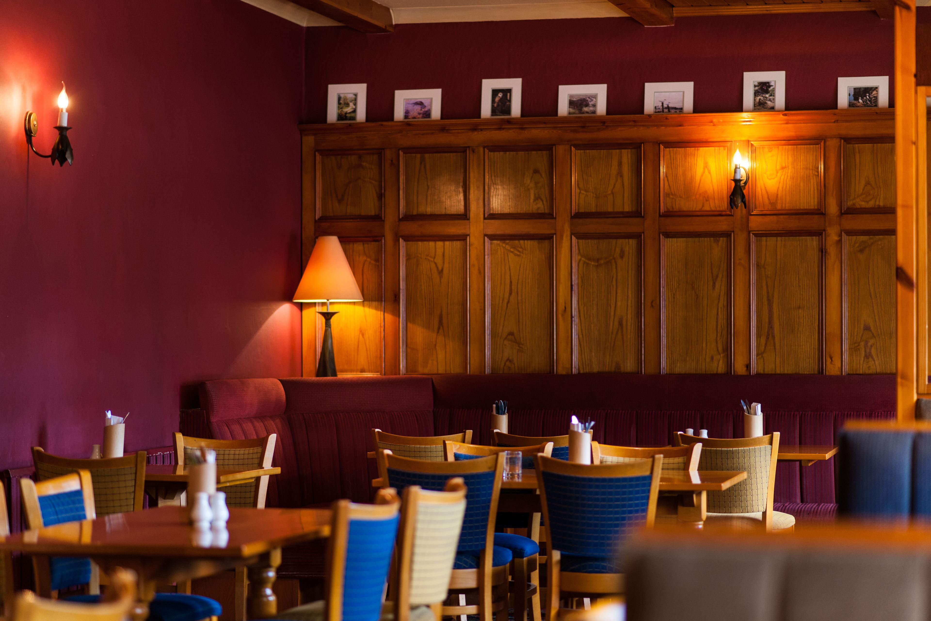 A restaurant interior with wooden panel walls, blue cushioned seating, and a warm-lit ambiance.