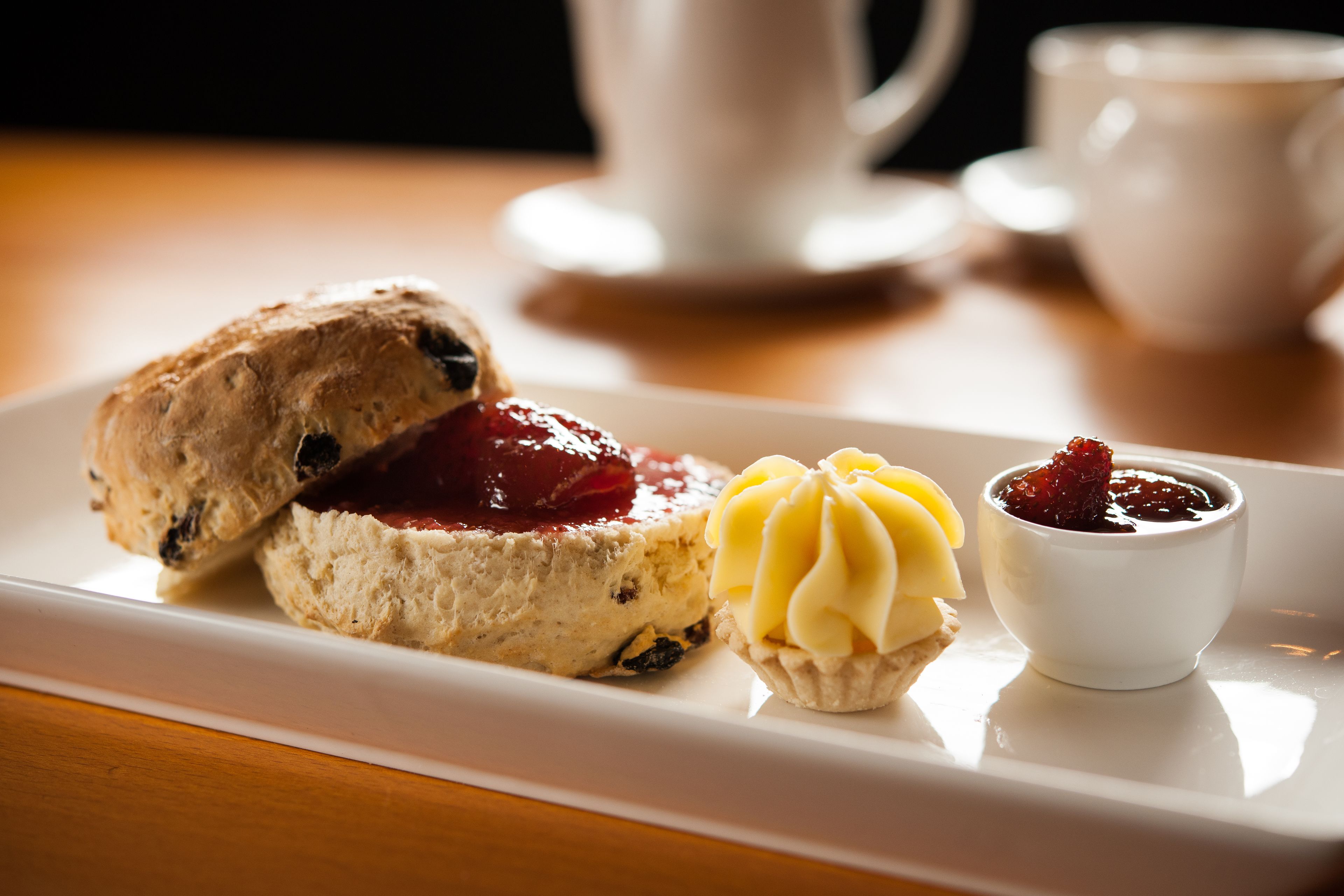 A white rectangular plate with a scone, a small tart, and a dollop of cream on a wooden table.