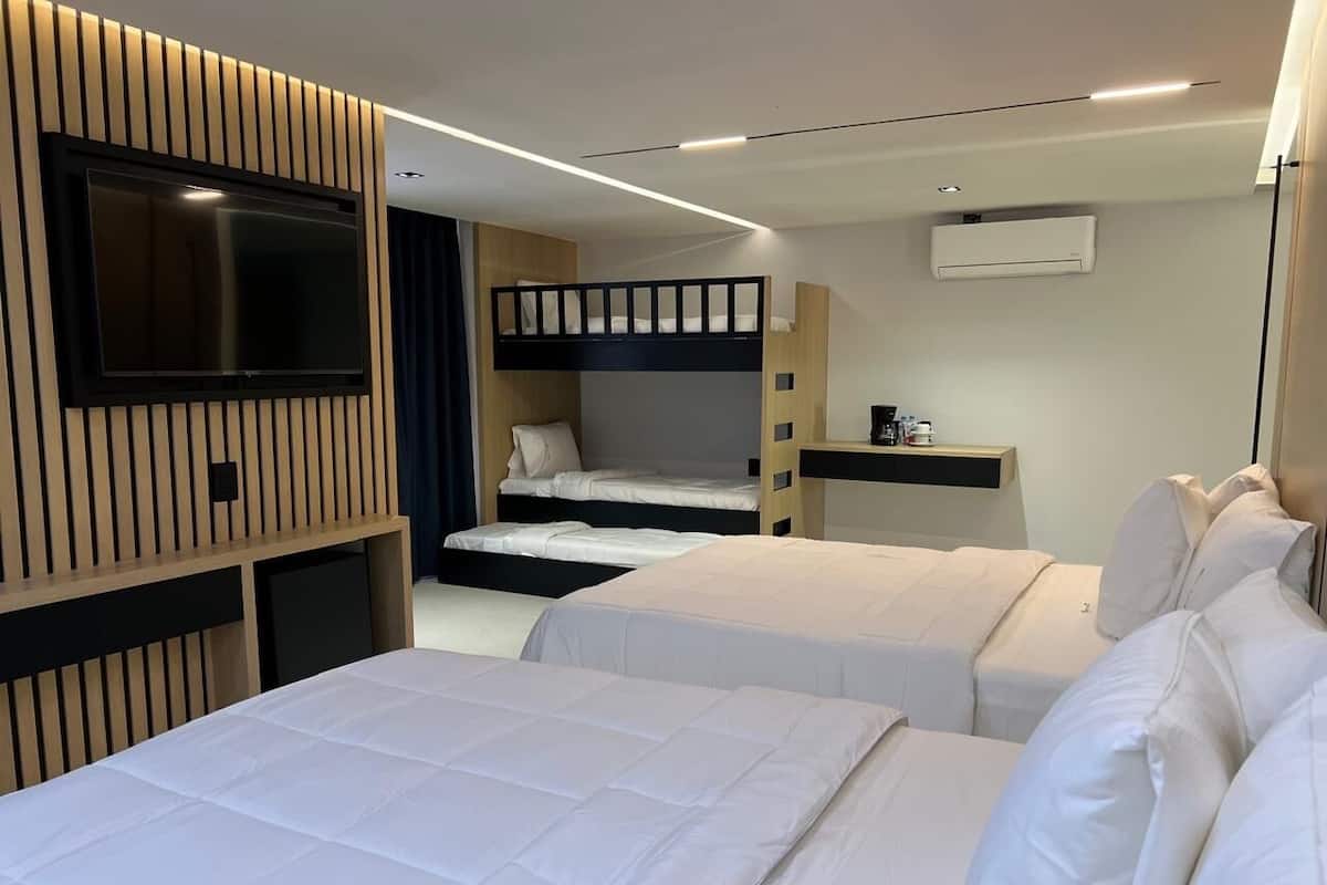 A hotel room with two beds, a TV mounted on the wall, and a bunk bed in the background.