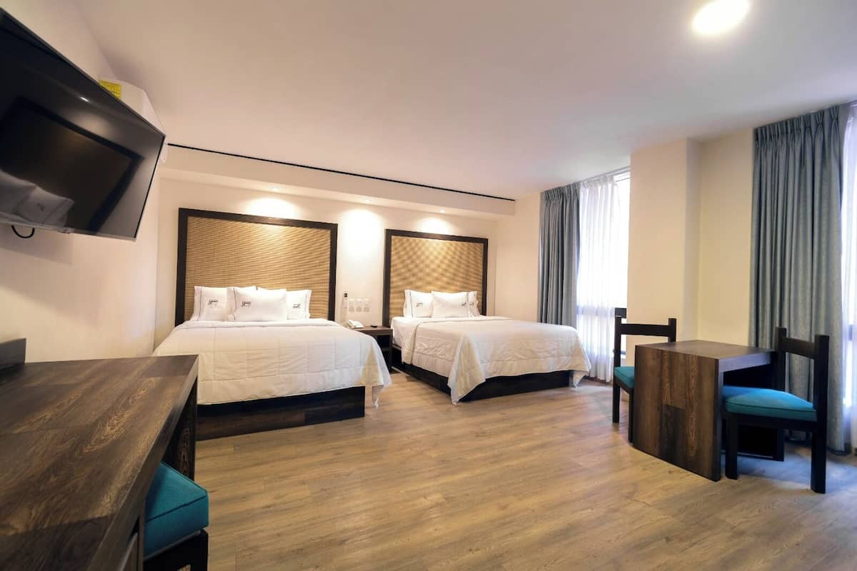 A hotel room with two beds, a desk, a chair, and a TV mounted on the wall.