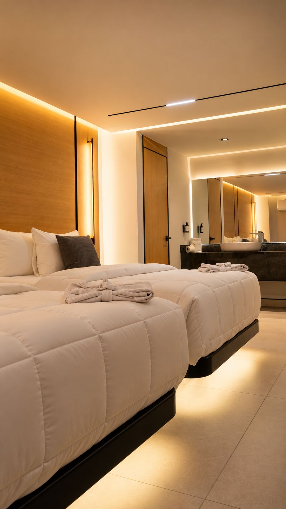 Una habitación de hotel moderna con una cama grande, una mesita de noche, un espejo y un baño con lavabo y espejo.