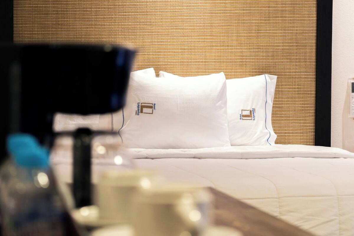 A hotel room with a bed, pillows, a nightstand, and a lamp.