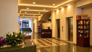 Un vestíbulo de hotel con mostrador de recepción, área de registro, un ascensor y una exhibición decorativa de objetos culturales.