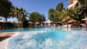 A swimming pool with blue tiles, surrounded by lounge chairs and umbrellas, with palm trees and a building in the background. - Valentin Somni Hotels & Suites – Adults Only +16 (Calvia)