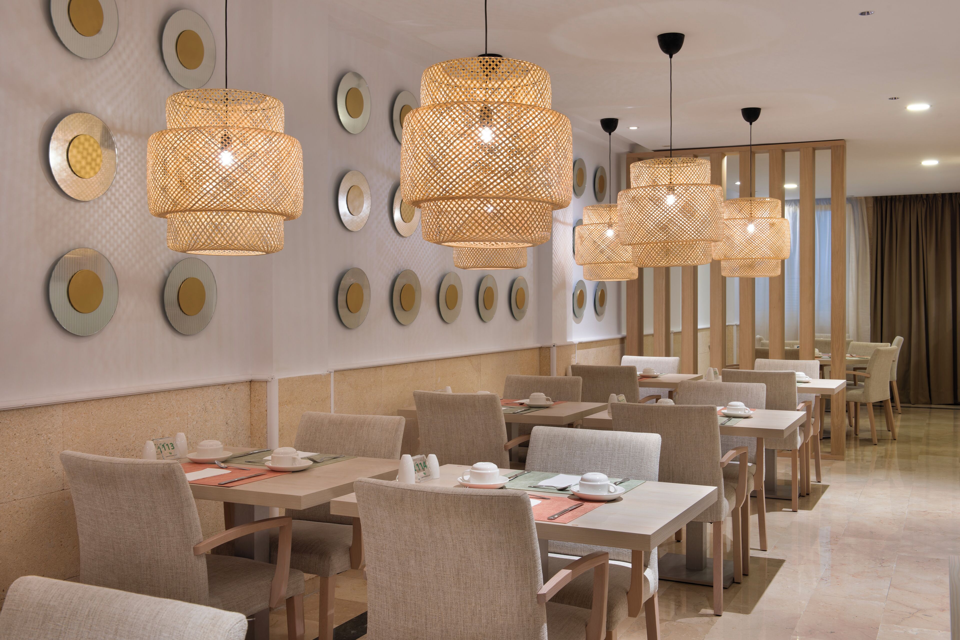 Un comedor moderno con varias mesas y sillas, paneles decorativos en la pared y lámparas colgantes de ratán.