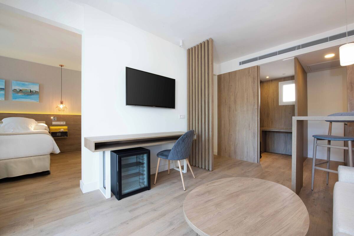 A modern hotel room with a bed, a desk with a chair, a television, and a small refrigerator.