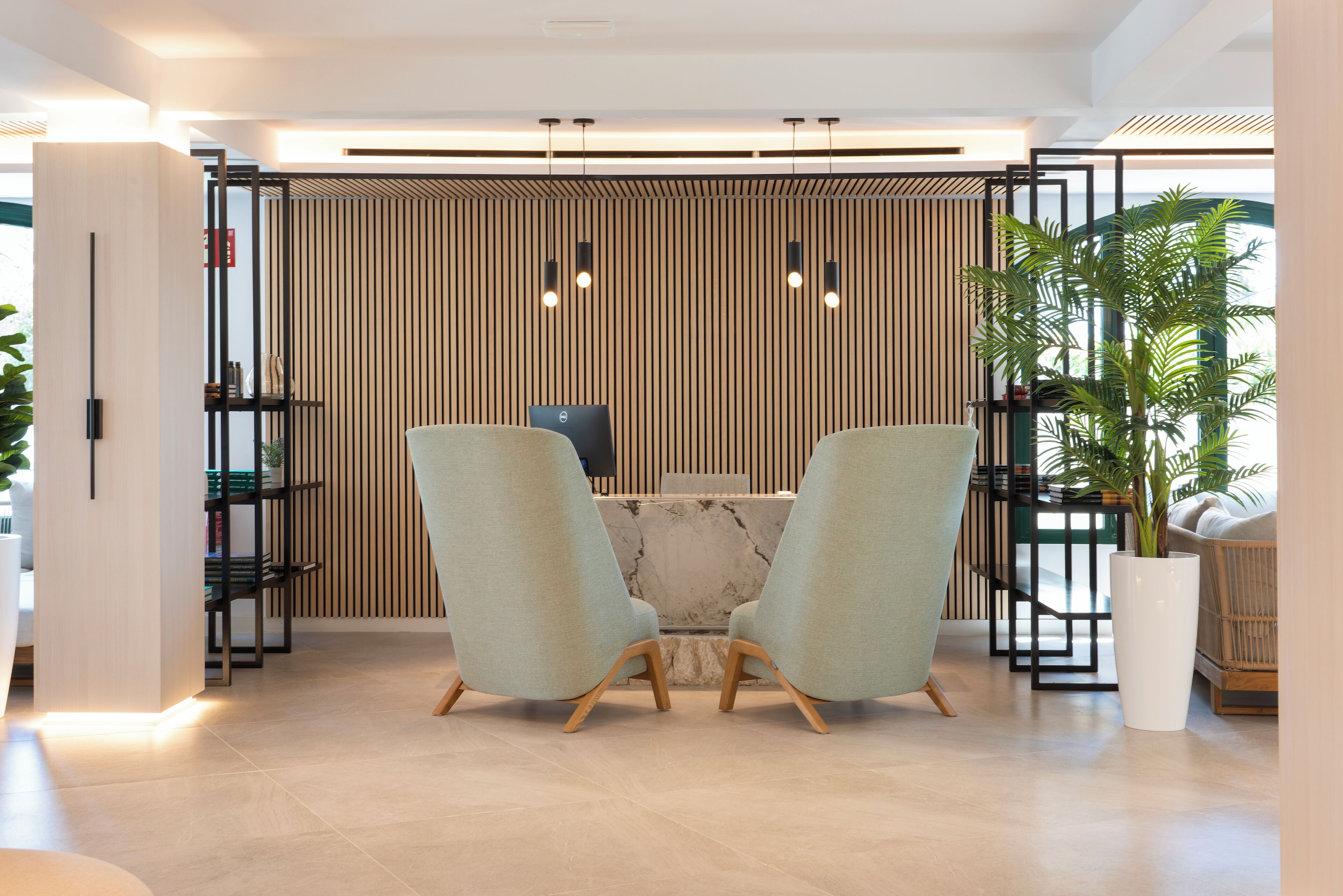 Un área de recepción moderna con dos sillas verde claro, una mesa de mármol y un panel de pared de madera vertical.