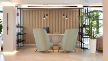 Un área de recepción moderna con dos sillas verde claro, una mesa de mármol y un panel de pared de madera vertical.