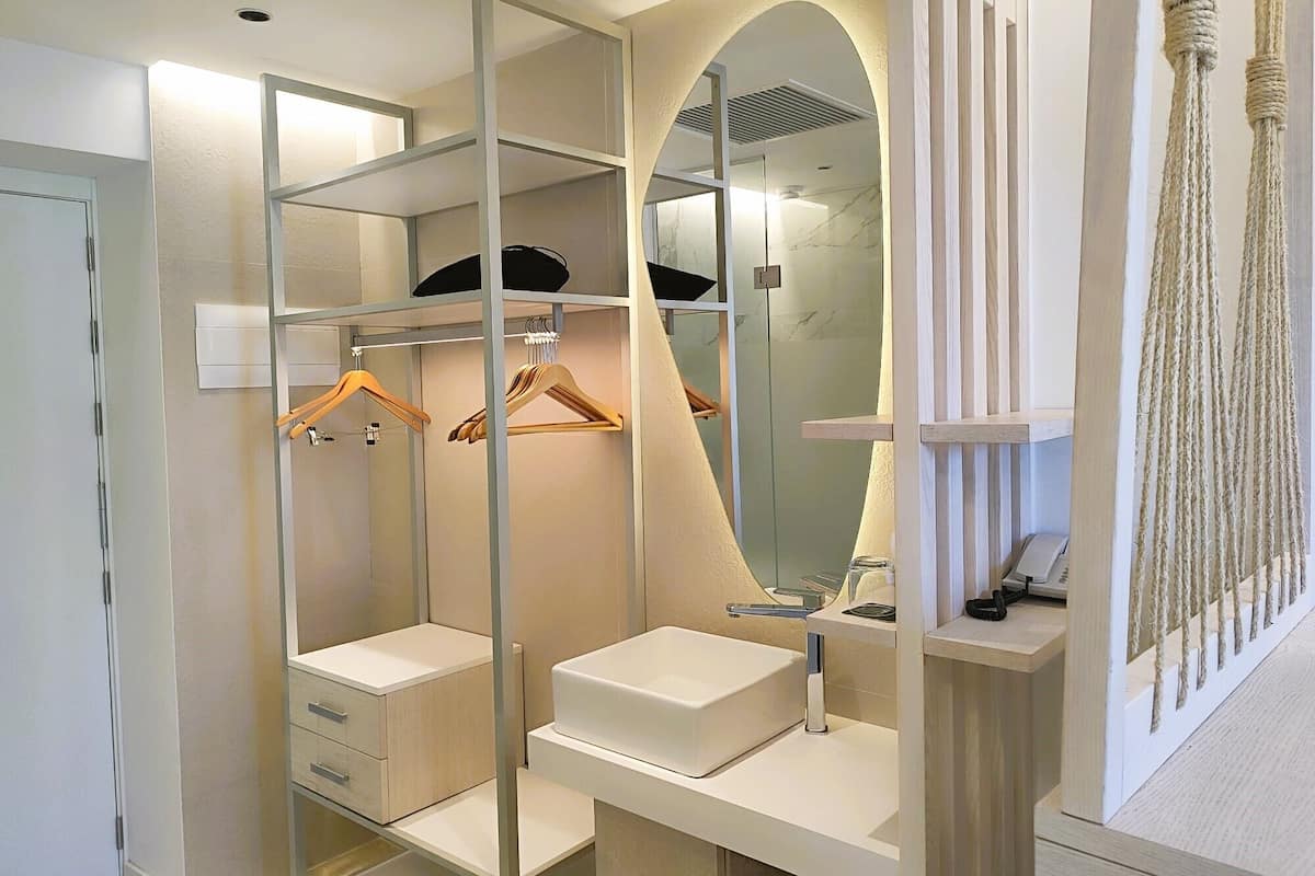 A modern bathroom with a walk-in closet, a vanity with a mirror, and a hanging macrame piece.