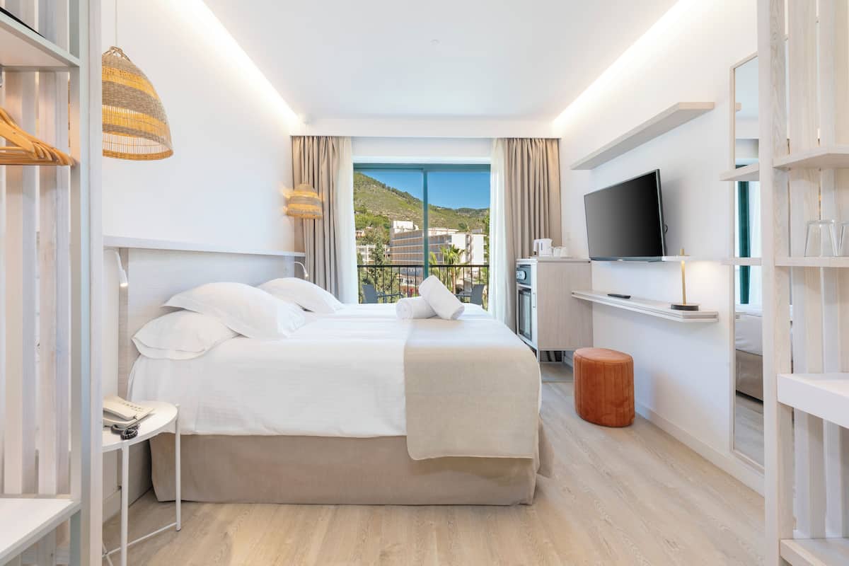 A modern hotel room with a large bed, a TV, a small table, and a view of the city.