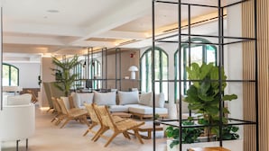 A modern living room with a sofa, chairs, and a coffee table. There are plants and a wooden shelf. - Valentin Somni Hotels & Suites – Adults Only +16 (Calvia)