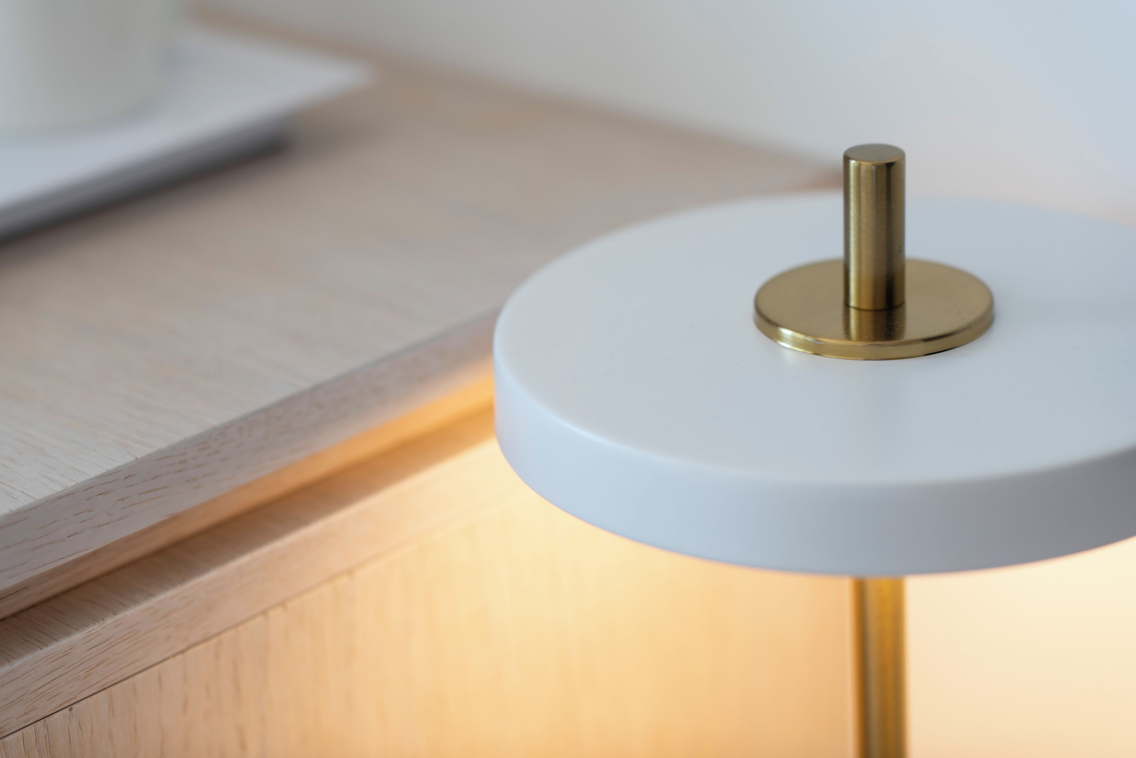 Primer plano de una lámpara de mesa moderna con base blanca y soporte color bronce.