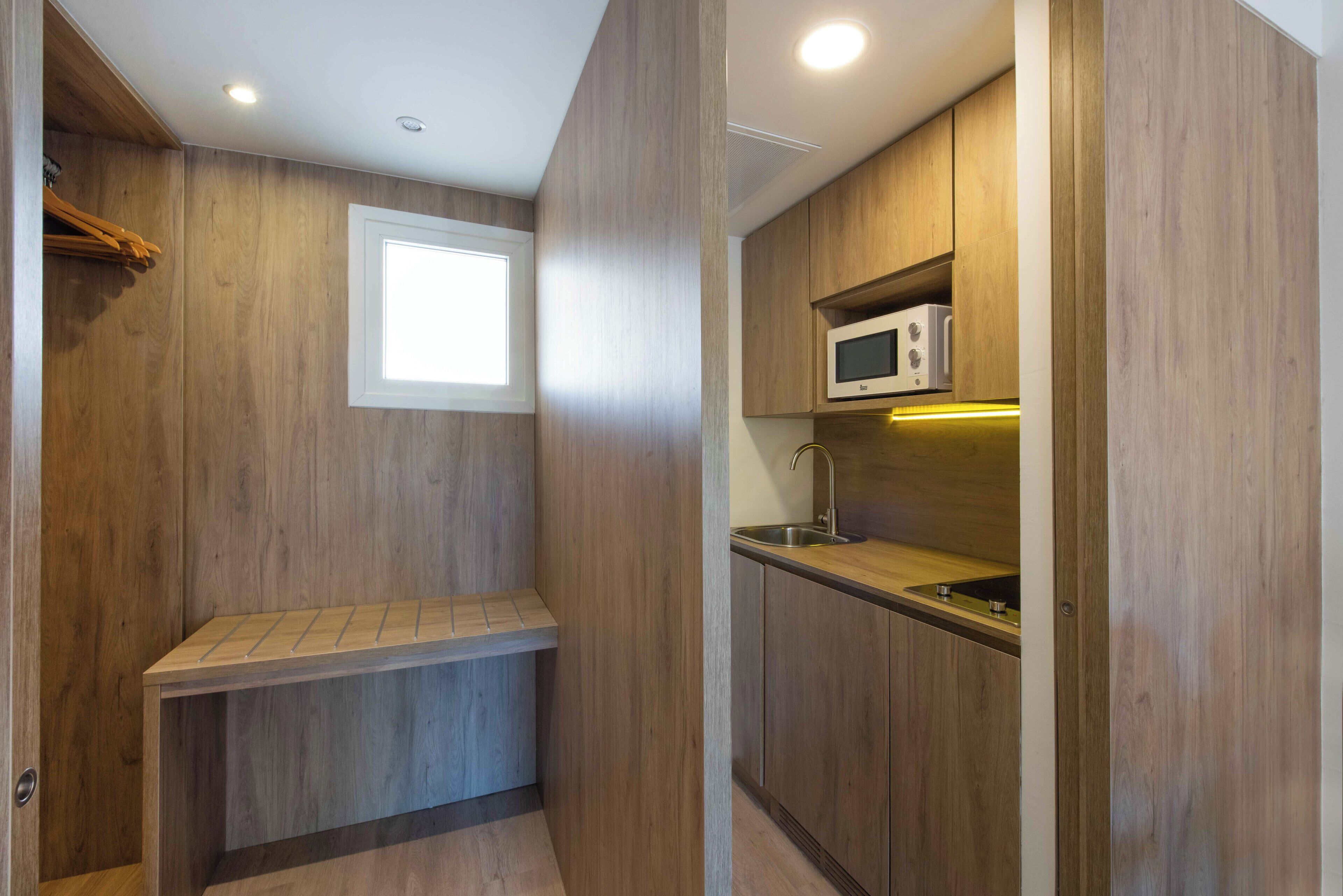 A compact kitchen with wooden cabinetry, a built-in microwave, and a window above the sink.