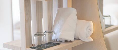 A wooden shelf with a rolled white towel, two glass containers, and a black coaster.