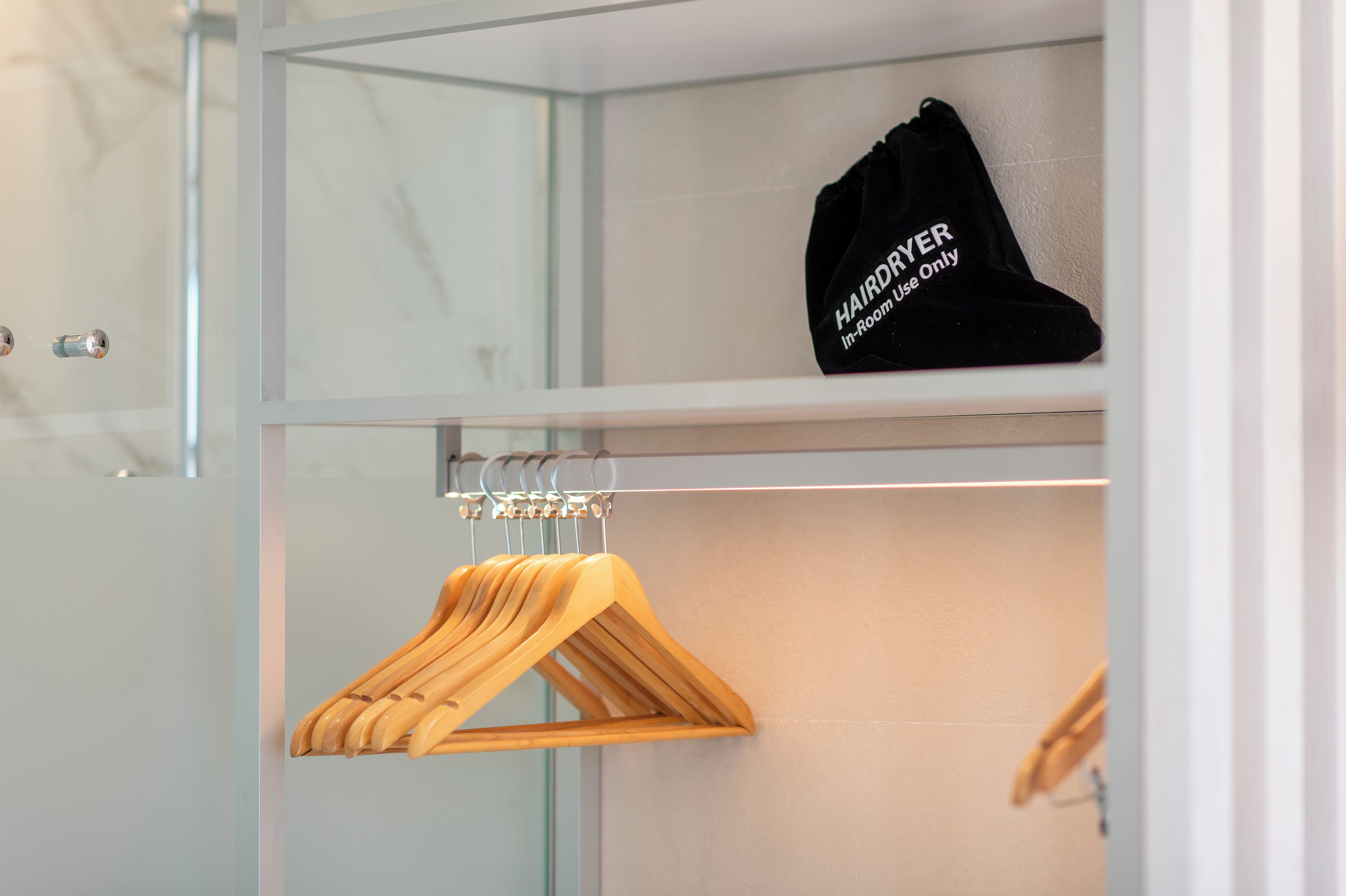 Een kast met houten kapstokken en een zwarte tas met het opschrift "HAIRDRYER In-Room Use Only".