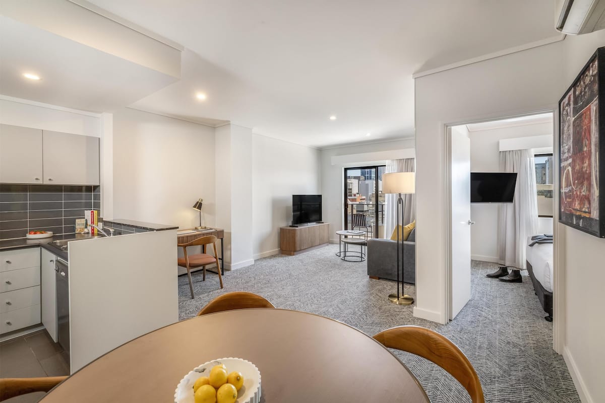 A modern hotel room with a dining area, kitchen, and living space.