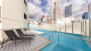 Une piscine sur le toit, dotée de chaises longues et offrant une vue sur la ville.