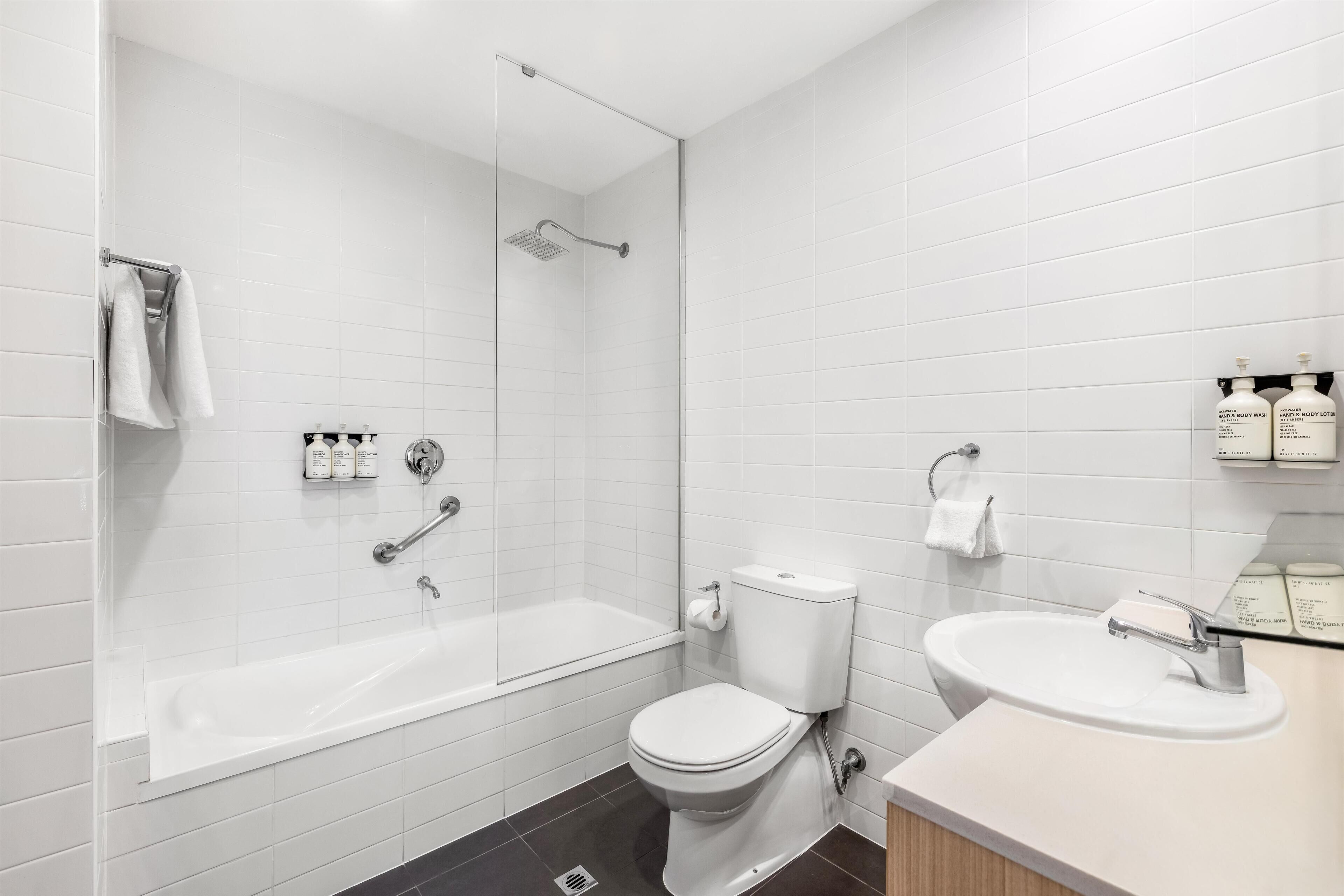 Une salle de bain moderne avec une douche à parois de verre, des toilettes blanches et un lavabo équipé de produits de toilette.