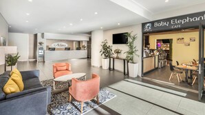 Un hall d’entrée moderne avec un comptoir d’accueil, un café appelé « Baby Elephant » et des espaces de détente.