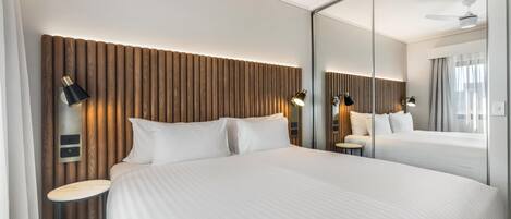 A hotel room with a large bed, a bedside table, a mirror, and a wall-mounted light fixture.