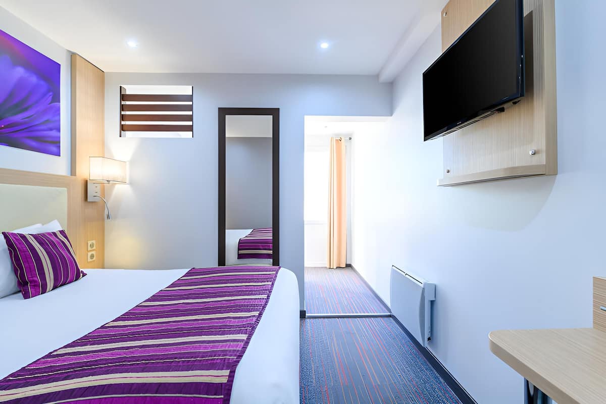 A hotel room with a bed, a TV, a mirror, a window, and a door.