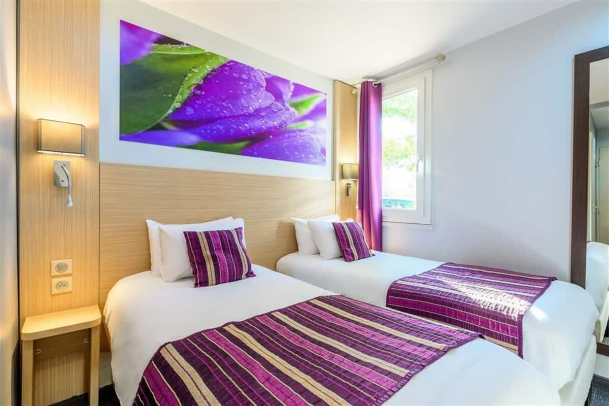 A hotel room with two beds, a large wall-mounted TV, and a window with curtains.