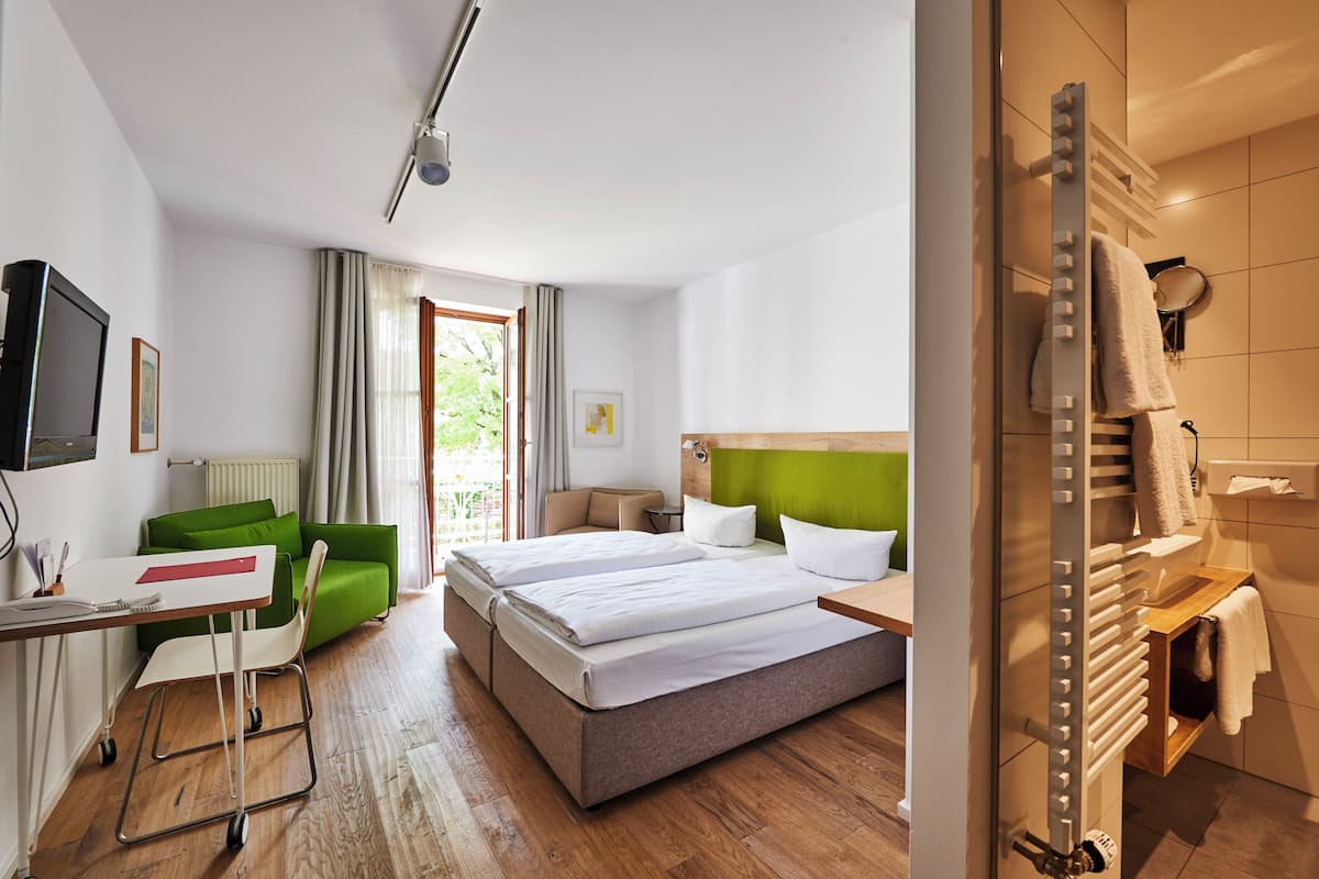 Habitación de hotel con cama, escritorio, silla, televisor y baño con perchero.