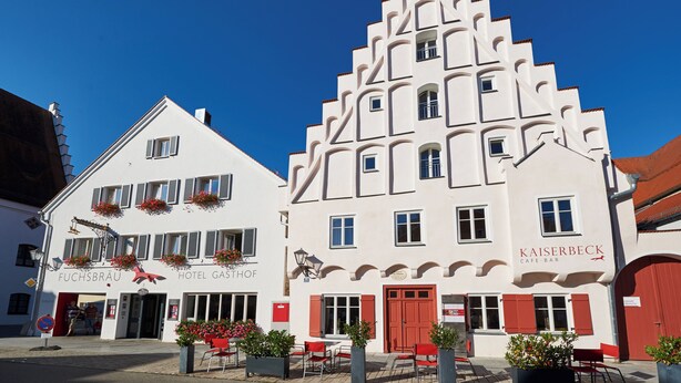 Un hotel de estilo arquitectónico europeo tradicional, con una entrada destacada que incluye una puerta roja y un letrero que anuncia 'Kaiserbeck Cafe-Bar'.